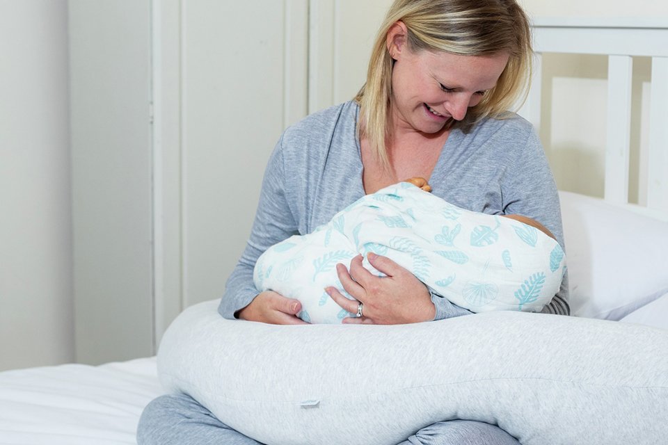 A mother using Purflo Breathe Pregnancy Firm Pillow in grey colour to feed her baby.